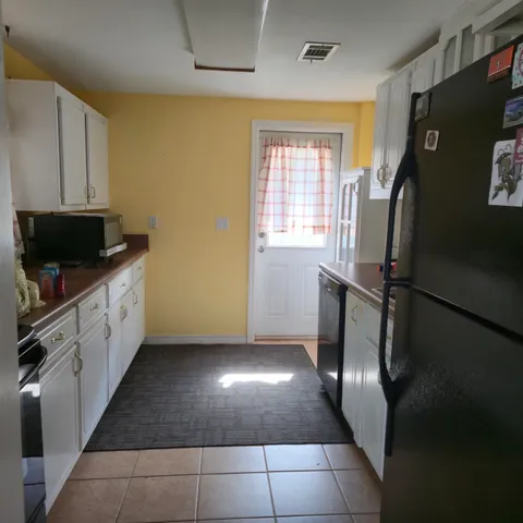 a view of a refrigerator in kitchen and an empty room with wooden floor