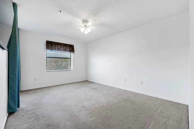 an empty room with chandelier fan and windows
