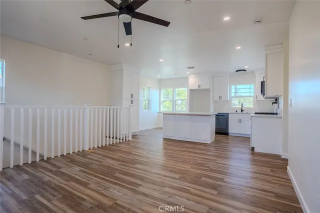 a view of an empty room and kitchen with wooden floor
