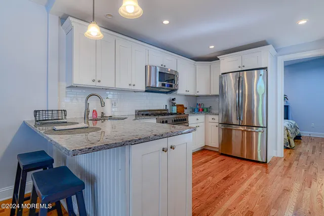 a kitchen with stainless steel appliances granite countertop a refrigerator a sink dishwasher a stove and white cabinets with wooden floor