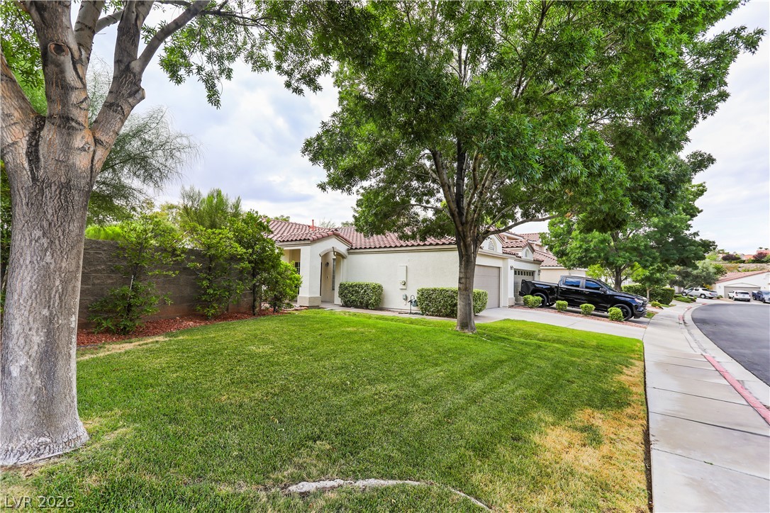 1134 Evening Ridge Street Henderson, NV 89052 - Photo 1 of 35 A well-maintained stucco residence with a terracotta tile roof, nestled among verdant trees and a manicured lawn.