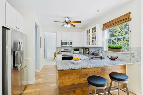 a kitchen with stainless steel appliances granite countertop a refrigerator a stove a sink a dining table and chairs with wooden floor