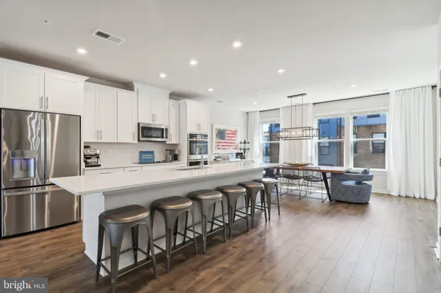 a kitchen with stainless steel appliances granite countertop a refrigerator a stove a sink a dining table and chairs with wooden floor