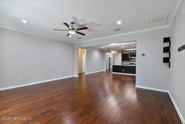a view of an empty room with kitchen window and wooden floor