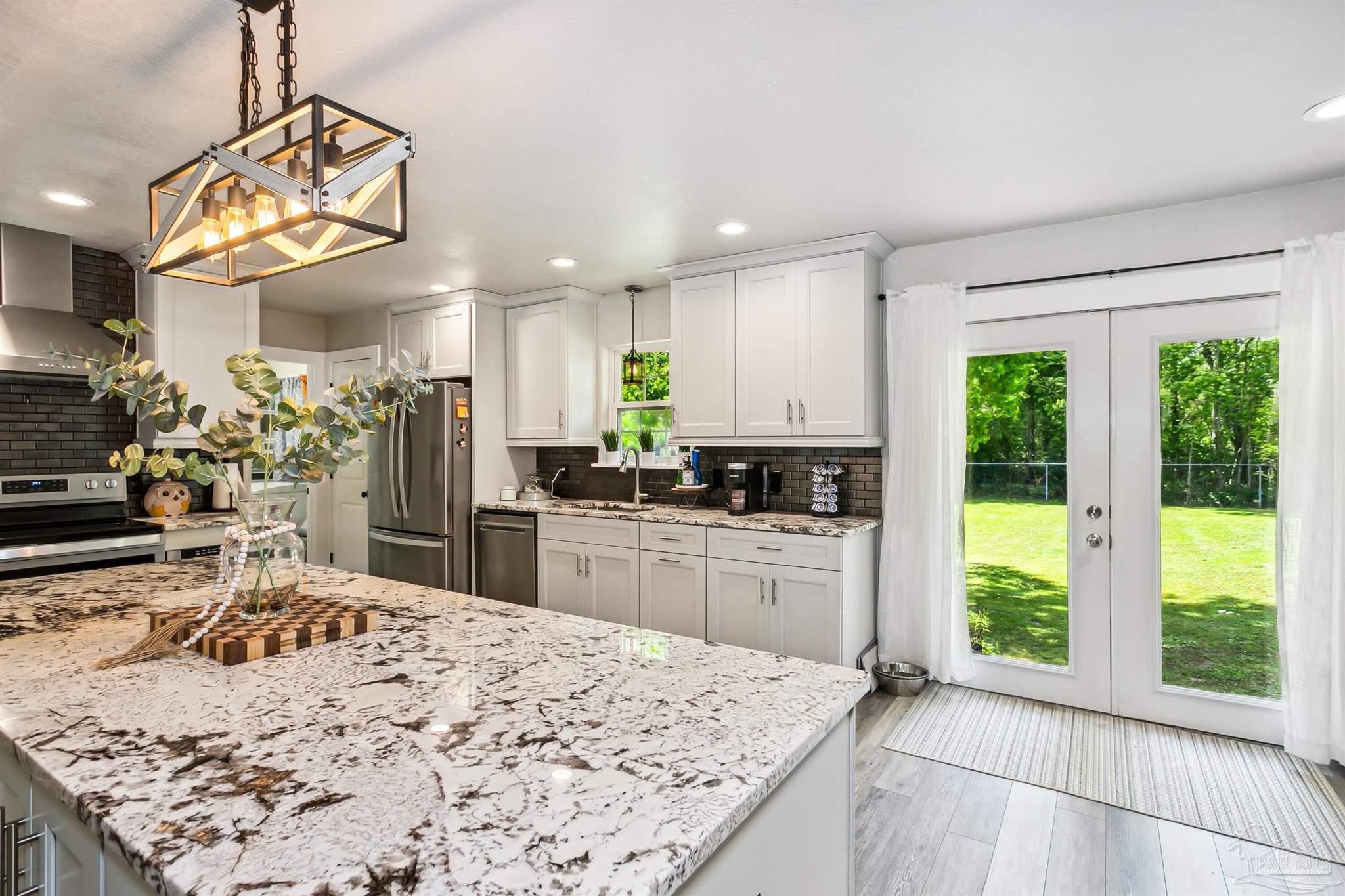 7260 Morrell Road Milton, FL 32583 - Photo 11 of 33 a kitchen with stainless steel appliances kitchen island granite countertop a refrigerator a sink dishwasher a stove and white cabinets with wooden floor