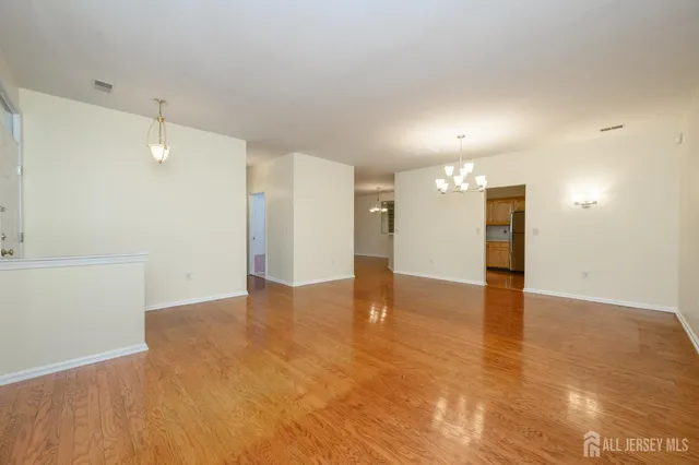 a view of an empty room with wooden floor and a kitchen