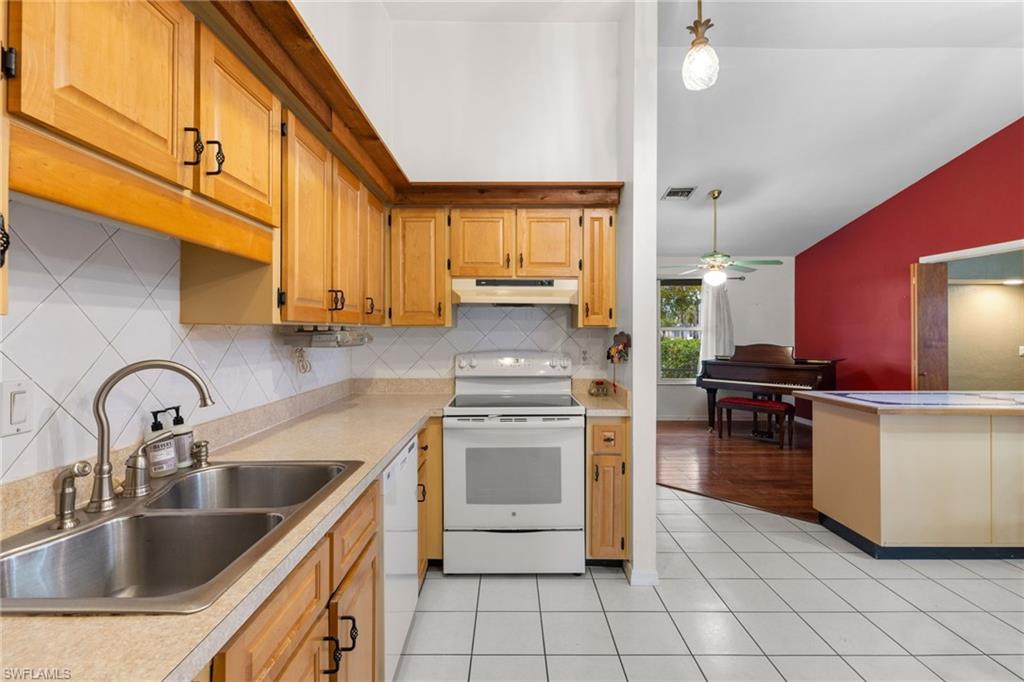 1700 42nd Terrace Southwest Naples, FL 34116 - Photo 10 of 27 Kitchen with white appliances, vaulted ceiling, light countertops, under cabinet range hood, and a sink