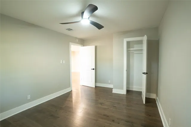 an empty room with wooden floor and a ceiling fan
