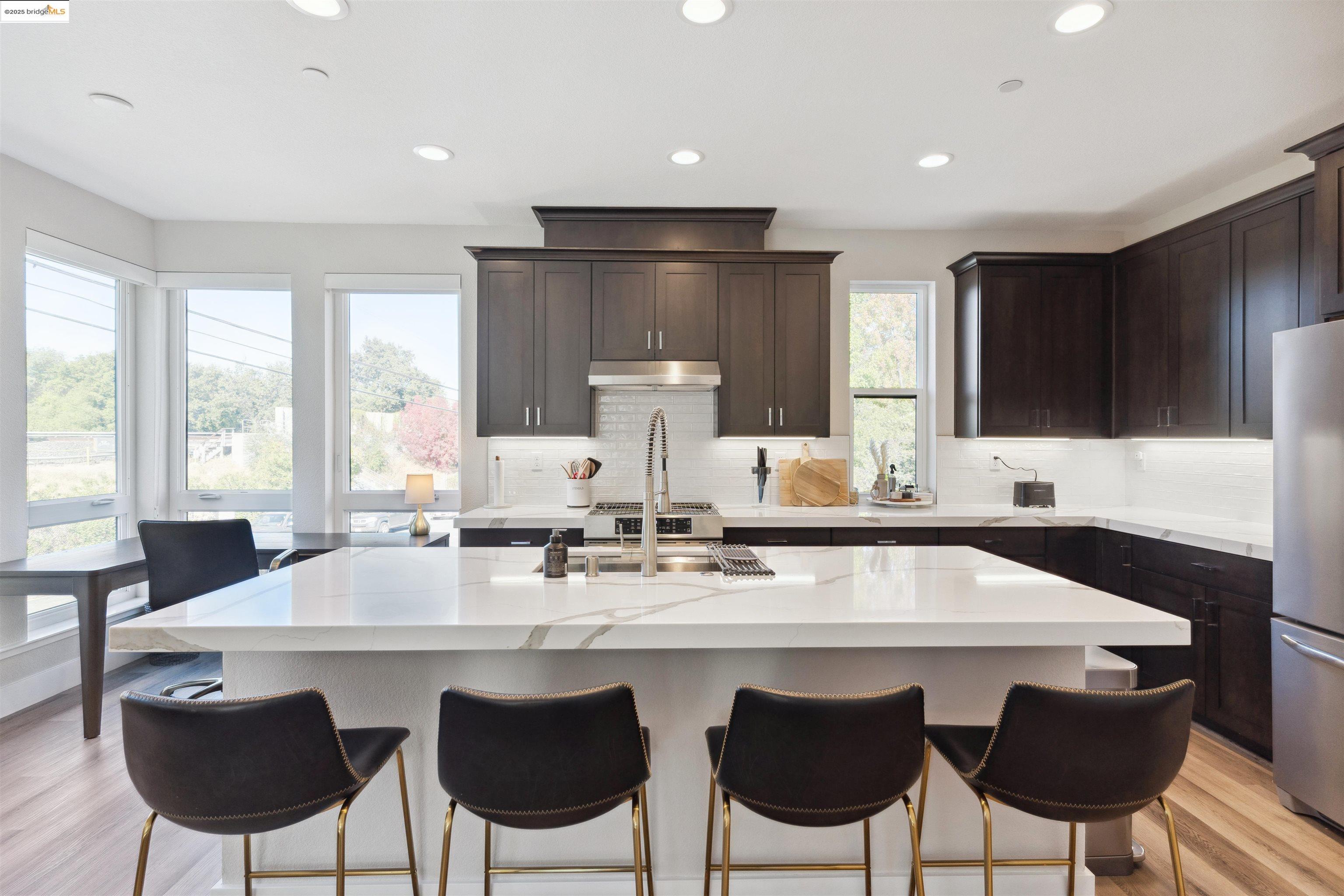 Kitchen with light wood-style floors, an island with sink, dark brown cabinetry, decorative backsplash, and recessed lighting