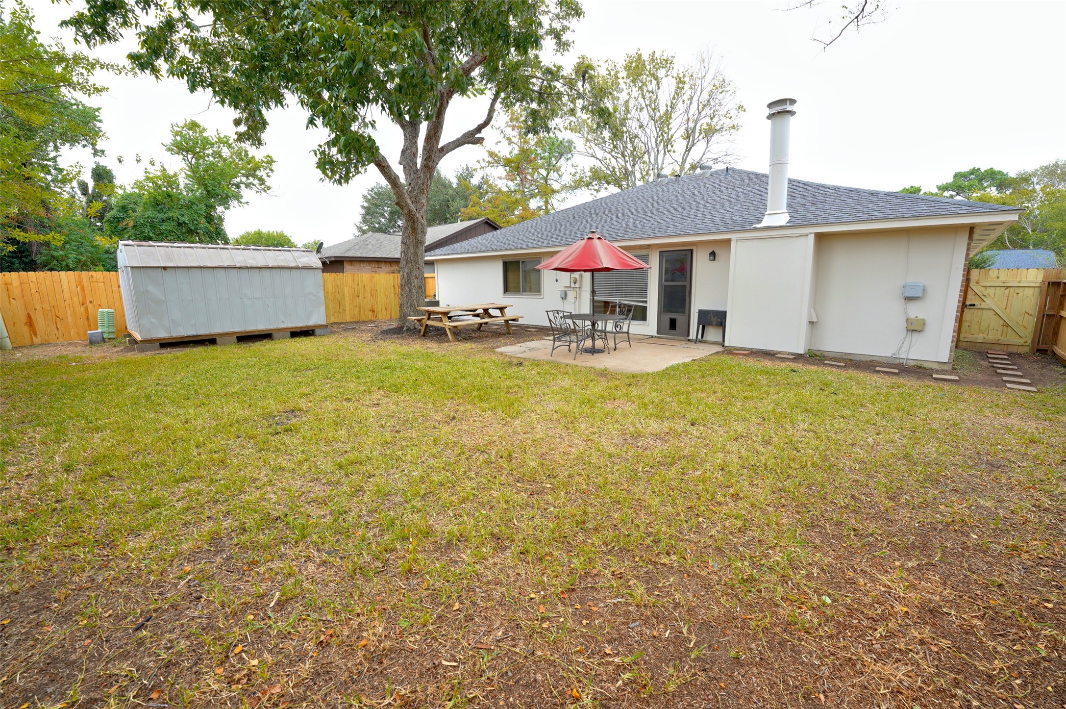 16715 Maplemont Drive Houston, TX 77095 - Photo 21 of 24 This photo showcases a spacious backyard featuring a patio area with outdoor seating and an umbrella, perfect for entertaining. The yard is fenced for privacy, includes a large tree for shade, and has a storage shed for extra space.