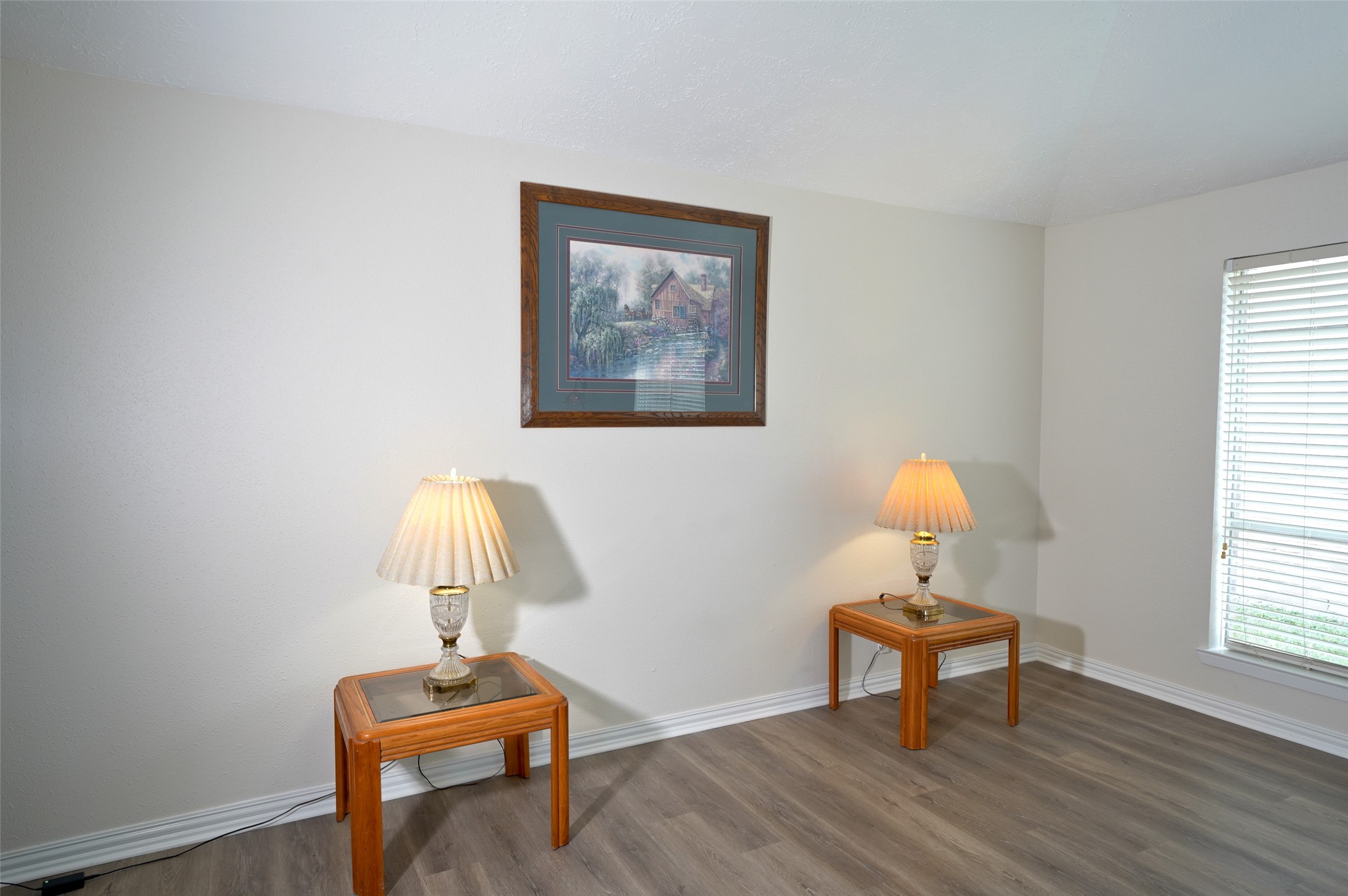 16715 Maplemont Drive Houston, TX 77095 - Photo 5 of 24 This room features light-colored walls and wood flooring, with two side tables and lamps creating a cozy ambiance. A large window provides natural light, and a framed picture adds a decorative touch.
