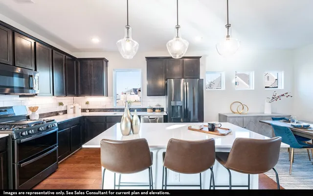 a kitchen with stainless steel appliances kitchen island granite countertop a dining table chairs sink and cabinets