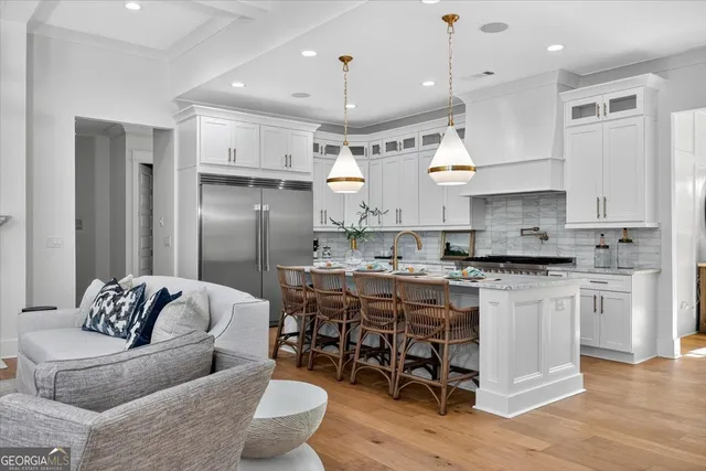 a large white kitchen with stainless steel appliances kitchen island granite countertop a dining table chairs and white cabinets