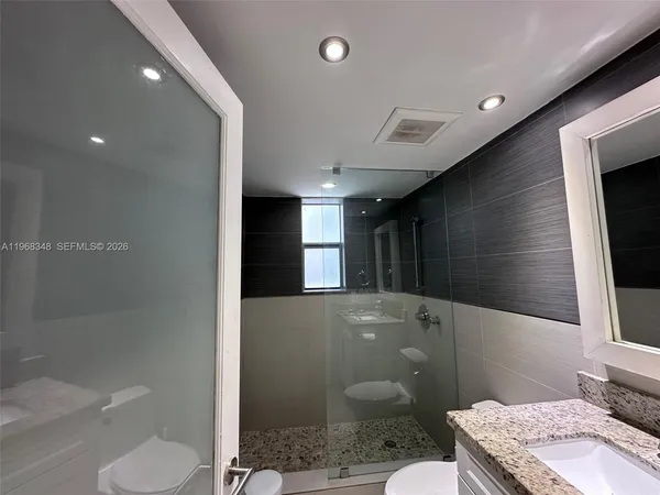 a bathroom with a granite countertop sink a toilet a mirror and shower