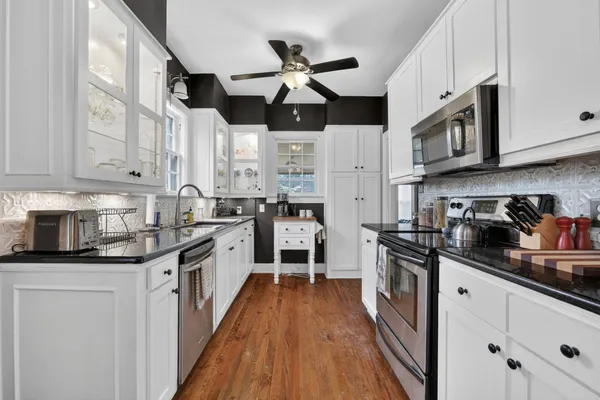 a kitchen with stainless steel appliances granite countertop white cabinets a sink a stove a refrigerator and island with wooden floor