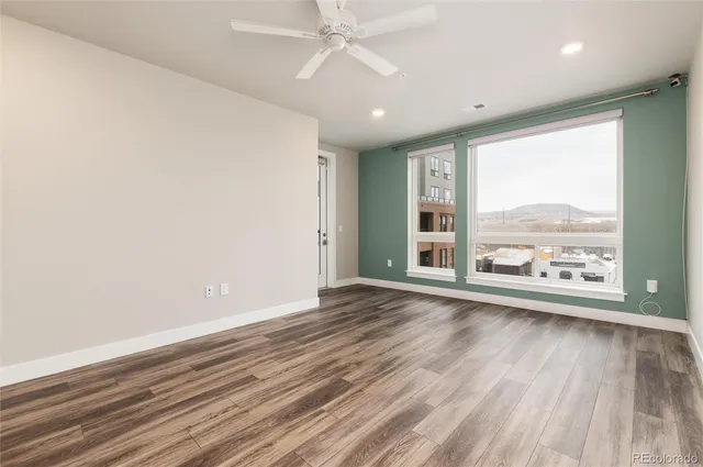 an empty room with wooden floor fan and windows