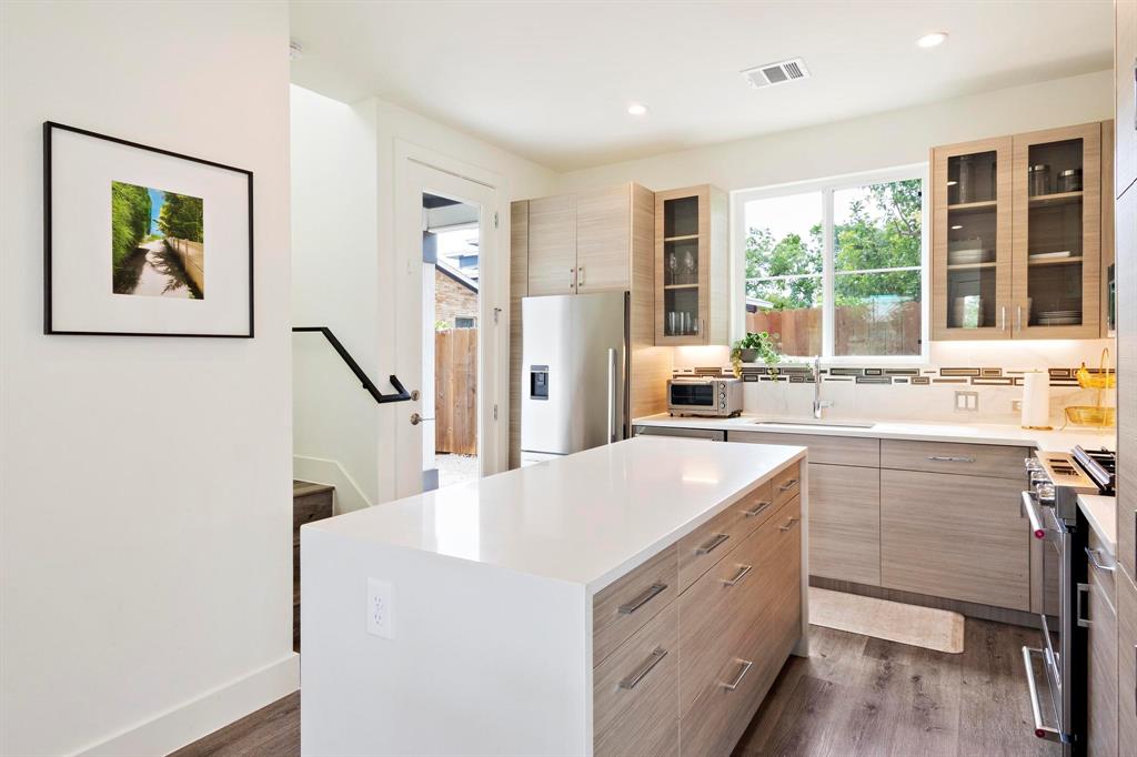 911 Stobaugh Street, Unit 2 Austin, TX 78757 - Photo 6 of 26 Modern kitchen featuring a central island with a white countertop, contemporary wood-finish cabinetry, stainless steel appliances, a large window, and recessed lighting