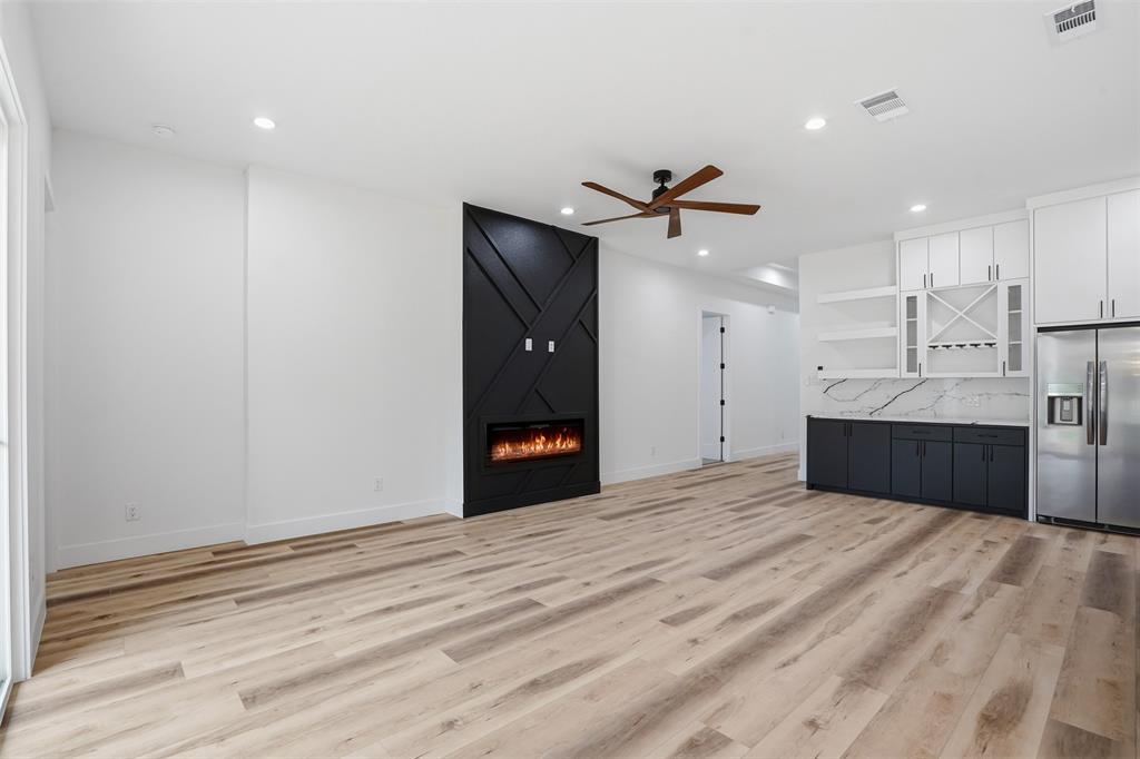 1111 Riverwood Road Dallas, TX 75217 - Photo 15 of 40 Spacious living area featuring light wood-finish flooring, a modern black accent wall with an electric fireplace, recessed lighting, and a ceiling fan