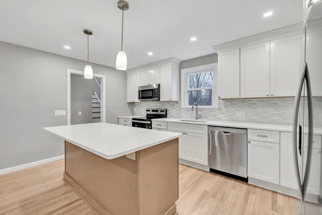 a kitchen with stainless steel appliances granite countertop a sink a stove a refrigerator and island with wooden floor