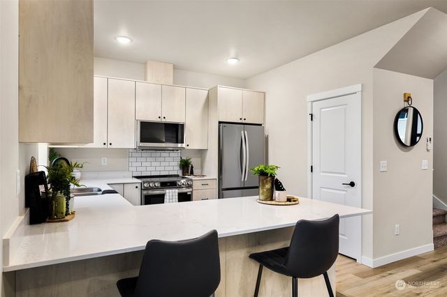 a kitchen with stainless steel appliances kitchen island granite countertop a refrigerator a stove a sink dishwasher and white cabinets with wooden floor