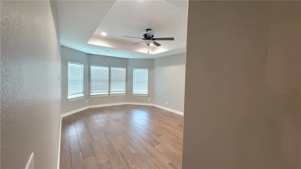 an empty room with wooden floor ceiling fan and windows