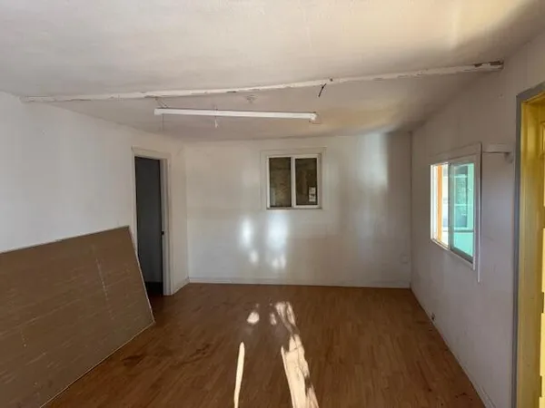 a view of an empty room with wooden floor and a window