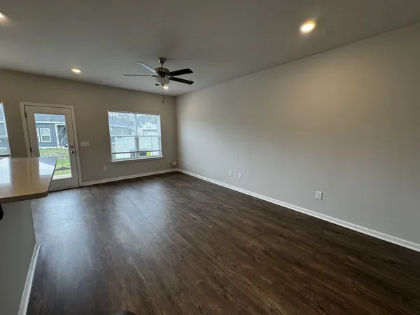 an empty room with wooden floor chandelier fan and windows