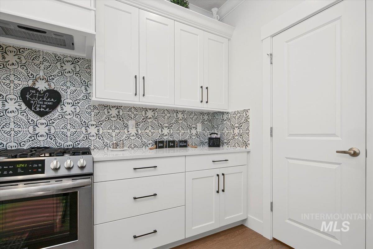 1685 Shoal Point Avenue Middleton, ID 83644 - Photo 15 of 44 Kitchen featuring stainless steel range with gas cooktop, white cabinetry, exhaust hood, decorative backsplash, and light stone countertops