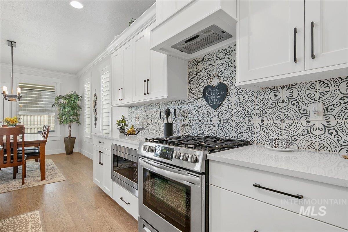 1685 Shoal Point Avenue Middleton, ID 83644 - Photo 17 of 44 Kitchen with stainless steel appliances, premium range hood, white cabinetry, light wood-type flooring, and ornamental molding