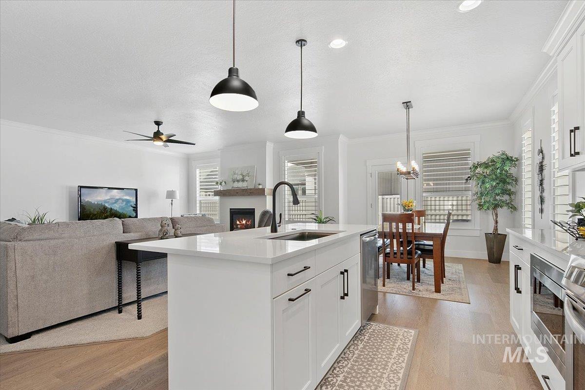 1685 Shoal Point Avenue Middleton, ID 83644 - Photo 19 of 44 Kitchen featuring a warm lit fireplace, white cabinets, hanging light fixtures, ornamental molding, and light wood-style floors