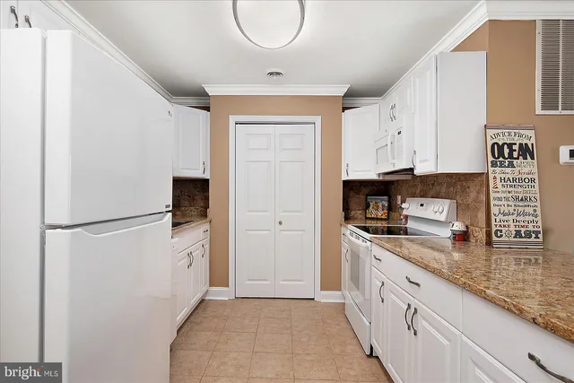 a kitchen with granite countertop a refrigerator a sink a stove and white cabinets