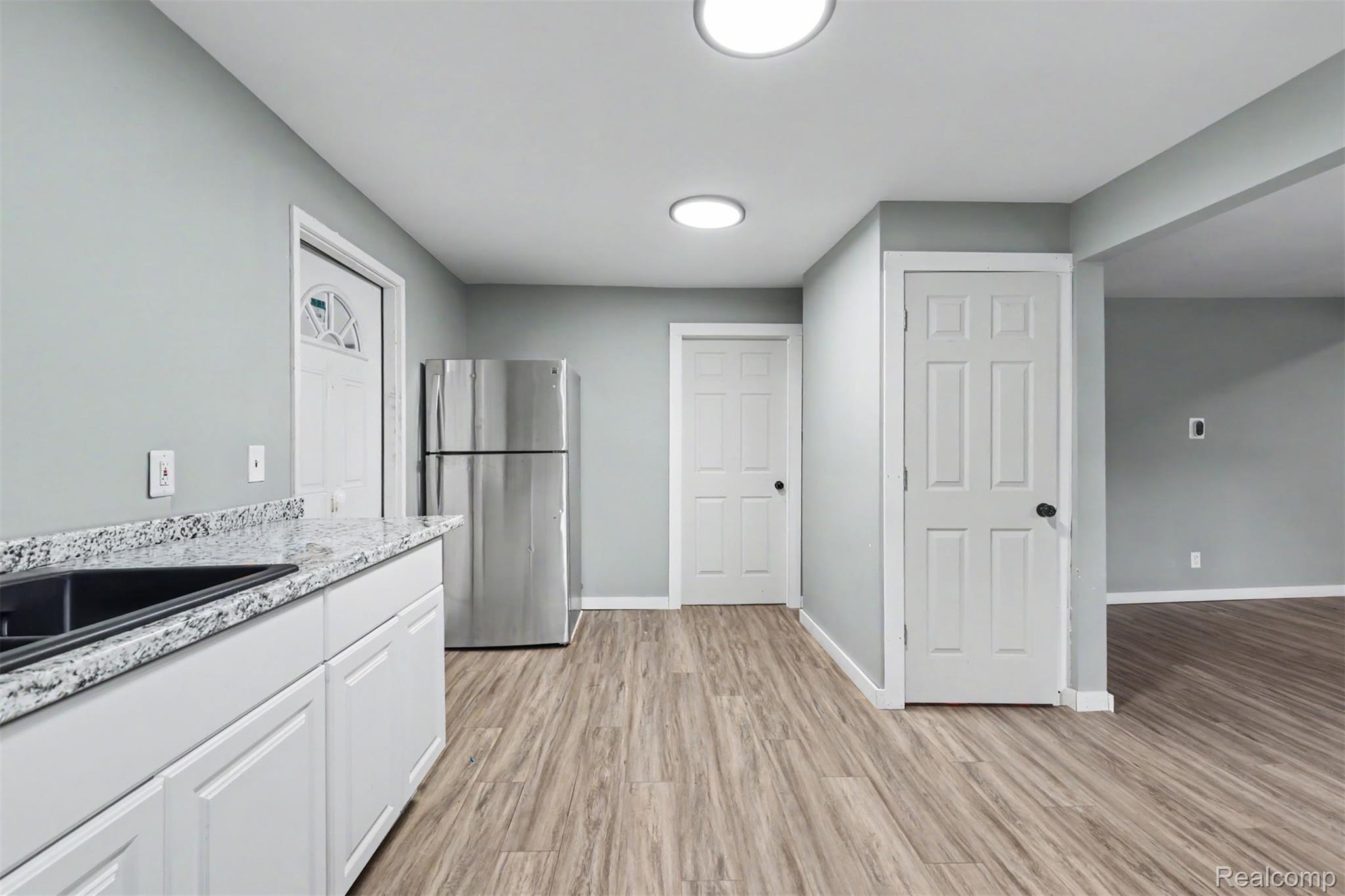 8397 Lane Street Detroit, MI 48209 - Photo 27 of 41 White cabinetry with a dark composite sink, light stone-finish countertop, stainless steel refrigerator, and wood-finish flooring