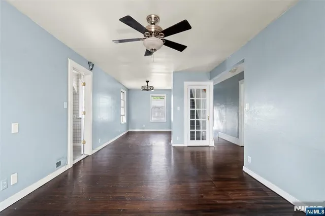 a view of an empty room with wooden floor and a ceiling fan