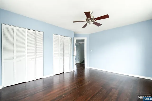a view of an empty room with wooden floor and a ceiling fan