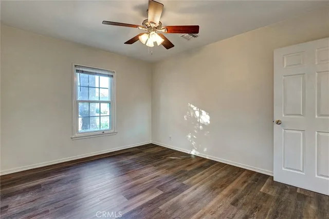 an empty room with wooden floor chandelier fan and windows