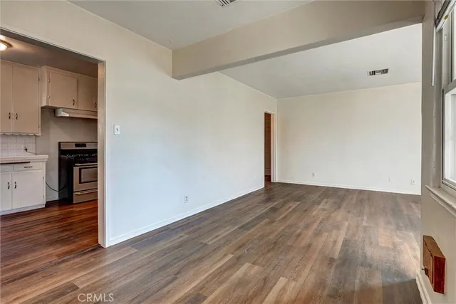 a view of empty room with wooden floor and kitchen