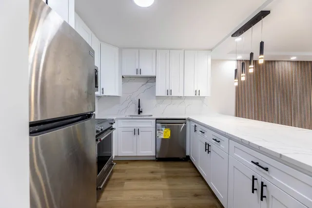 a kitchen with granite countertop a refrigerator a sink and white cabinets
