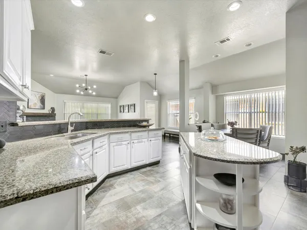 an open kitchen with granite countertop a sink and white cabinets with wooden floor