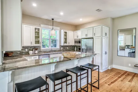 a kitchen with stainless steel appliances granite countertop a stove a sink a refrigerator white cabinets and wooden floor