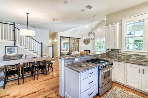 a kitchen with granite countertop a stove a sink a dining table and chairs with wooden floor