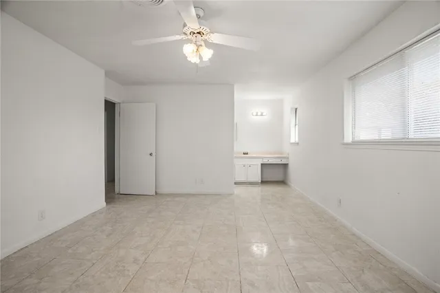 an empty room with chandelier fan and windows