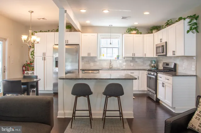 a kitchen with stainless steel appliances granite countertop a stove a sink a refrigerator and white cabinets with wooden floor