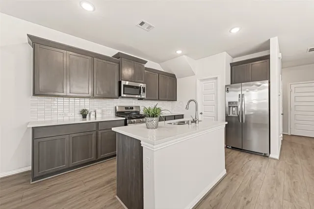 a kitchen with stainless steel appliances granite countertop a refrigerator a sink dishwasher a stove with wooden cabinets and floors