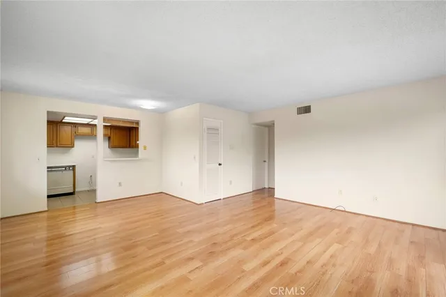 a view of empty room with wooden floor and kitchen