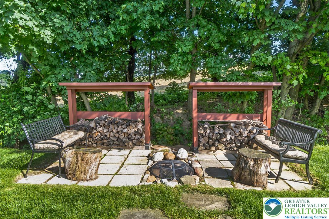 540 Briar Road Pen Argyl, PA 18072 - Photo 51 of 66 outdoor fire pit area, flanked by wood storage and garden benches, offers a charming spot for gatherings.