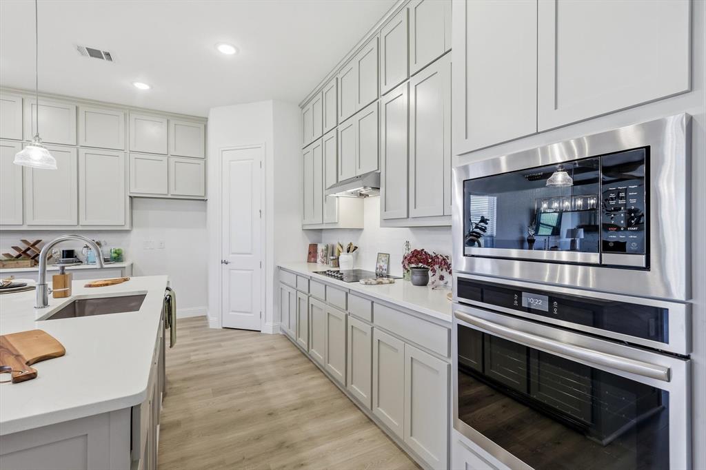 4017 Eagles Bluff Road Midlothian, TX 76065 - Photo 18 of 38 Modern kitchen featuring light cabinetry, stainless steel appliances, quartz countertops, a kitchen island with an undermount sink, and wood-finish flooring