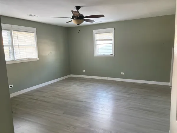 an empty room with wooden floor ceiling fan and windows