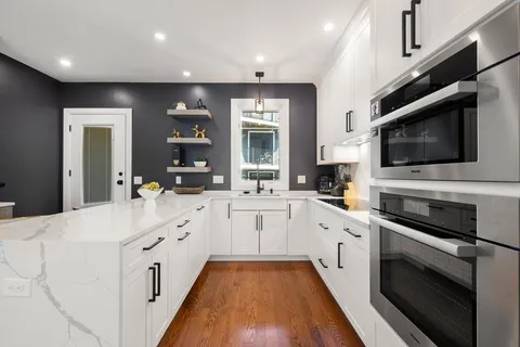 a large white kitchen with stainless steel appliances granite countertop a stove and a sink