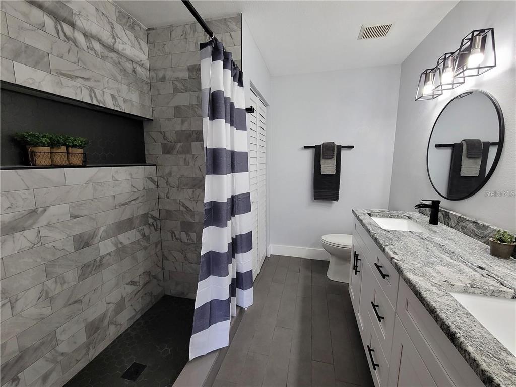 1801 East Lake Road South, Unit 15E Palm Harbor, FL 34685 - Photo 11 of 24 a spacious bathroom with a granite countertop toilet a sink and a mirror