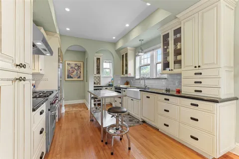 a open kitchen with granite countertop a stove a sink a dining table and chairs with wooden floor